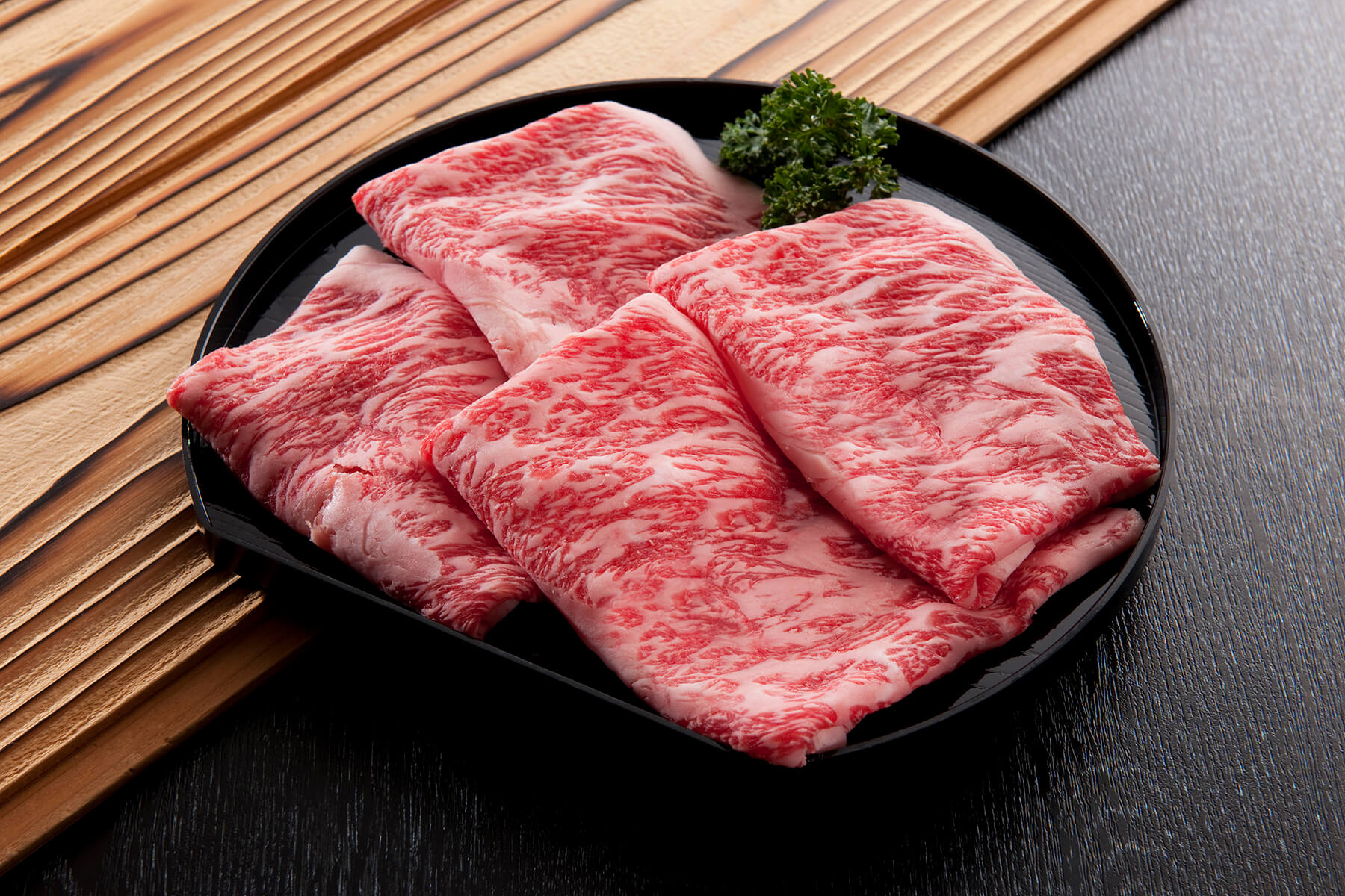 Thinly sliced marbled Wagyu beef on a black plate