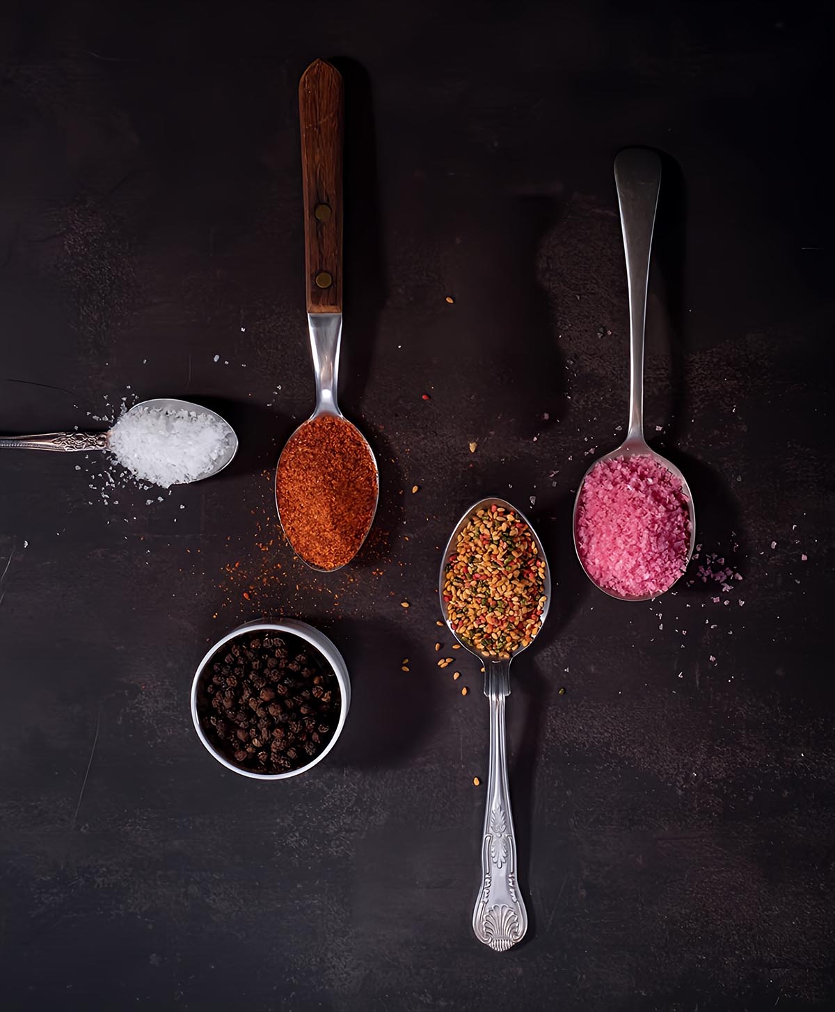 Assorted seasonings in spoons on a dark surface
